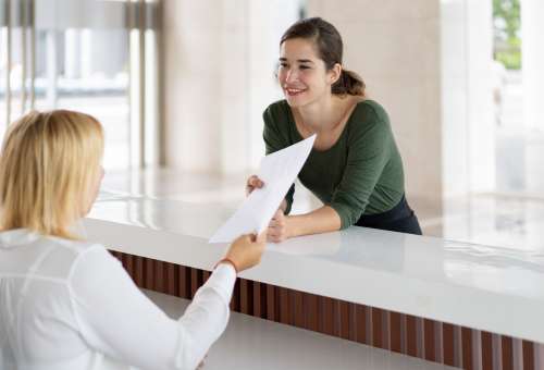 Front desk lady offering tourist to fill out documents. Receptionist giving papers to smiling hotel guest. Hotel and check in concept
